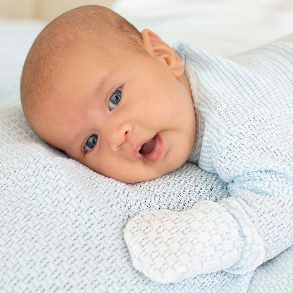 Newborn baby lying on a textured blanket wearing a light blue outfit.
