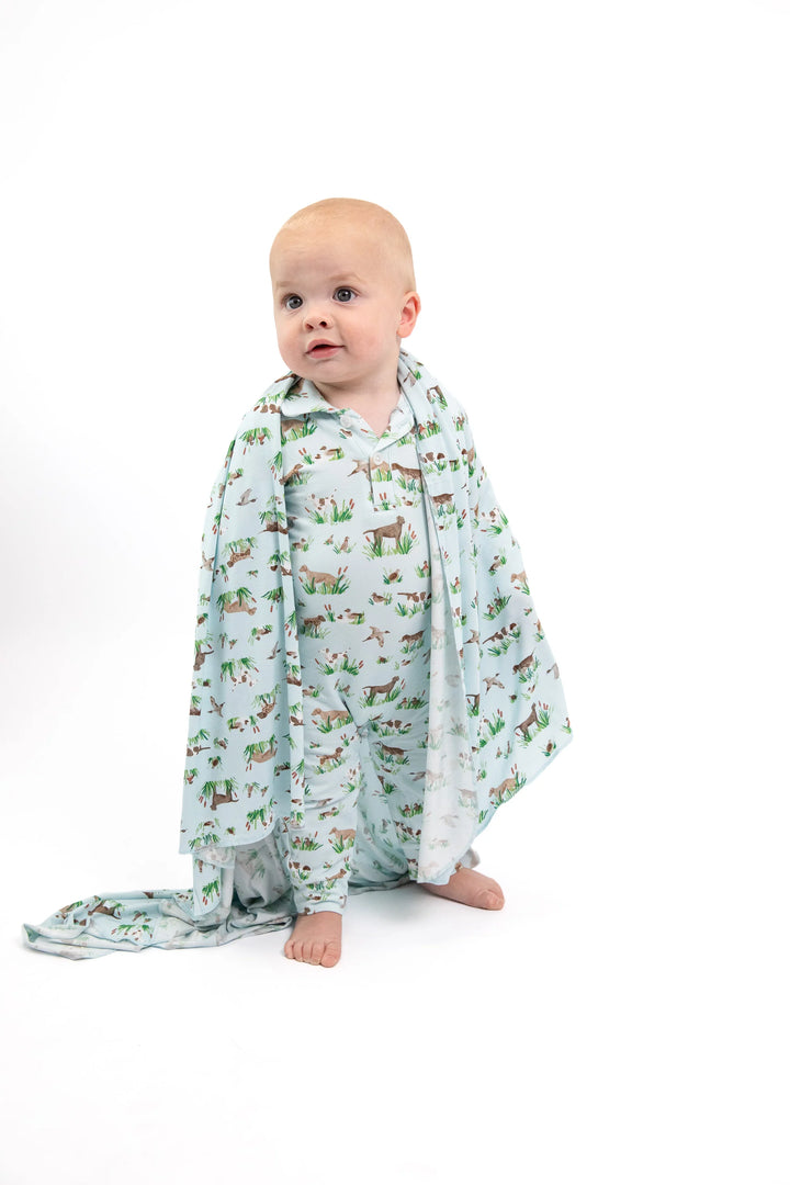 A baby sitting on a white studio background wearing a long-sleeve button-up pajama shirt and a matching printed blanket or wrap with woodland animals.