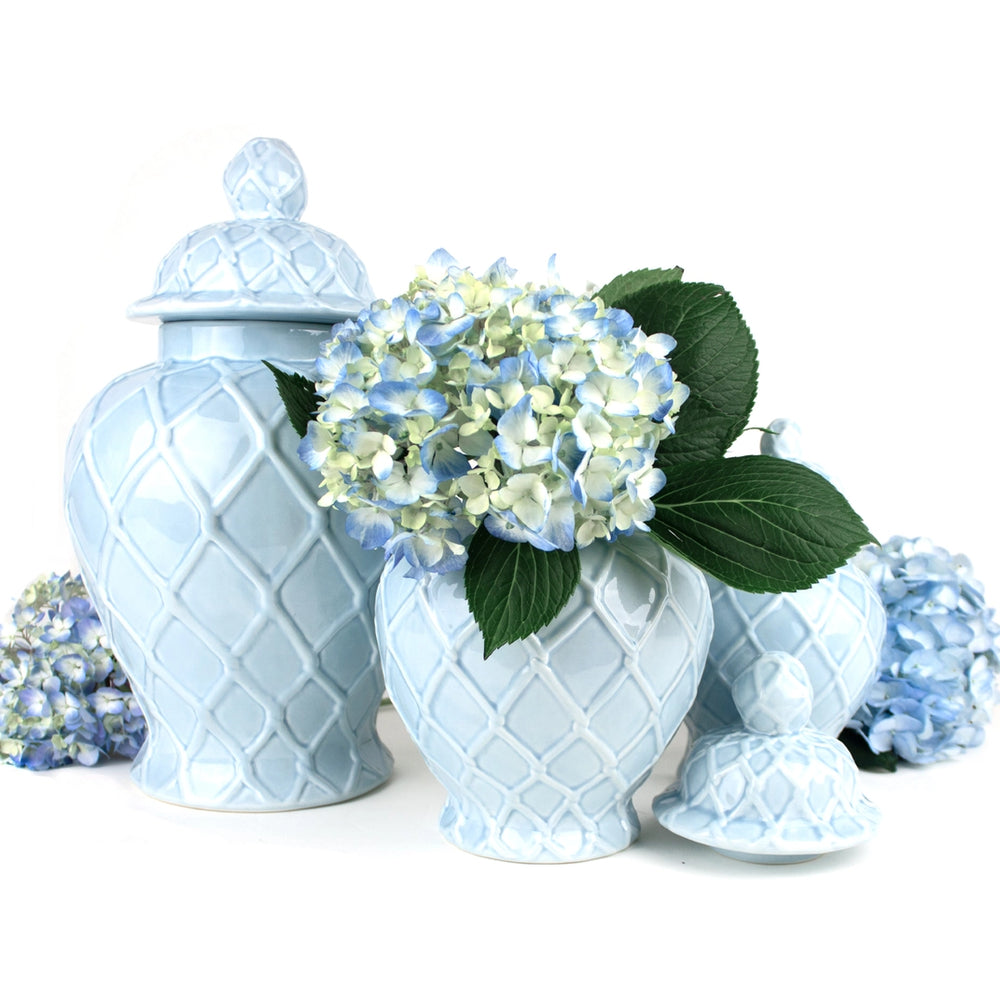 Light blue ceramic urns with decorative patterns and a small bouquet of flowers on a white background