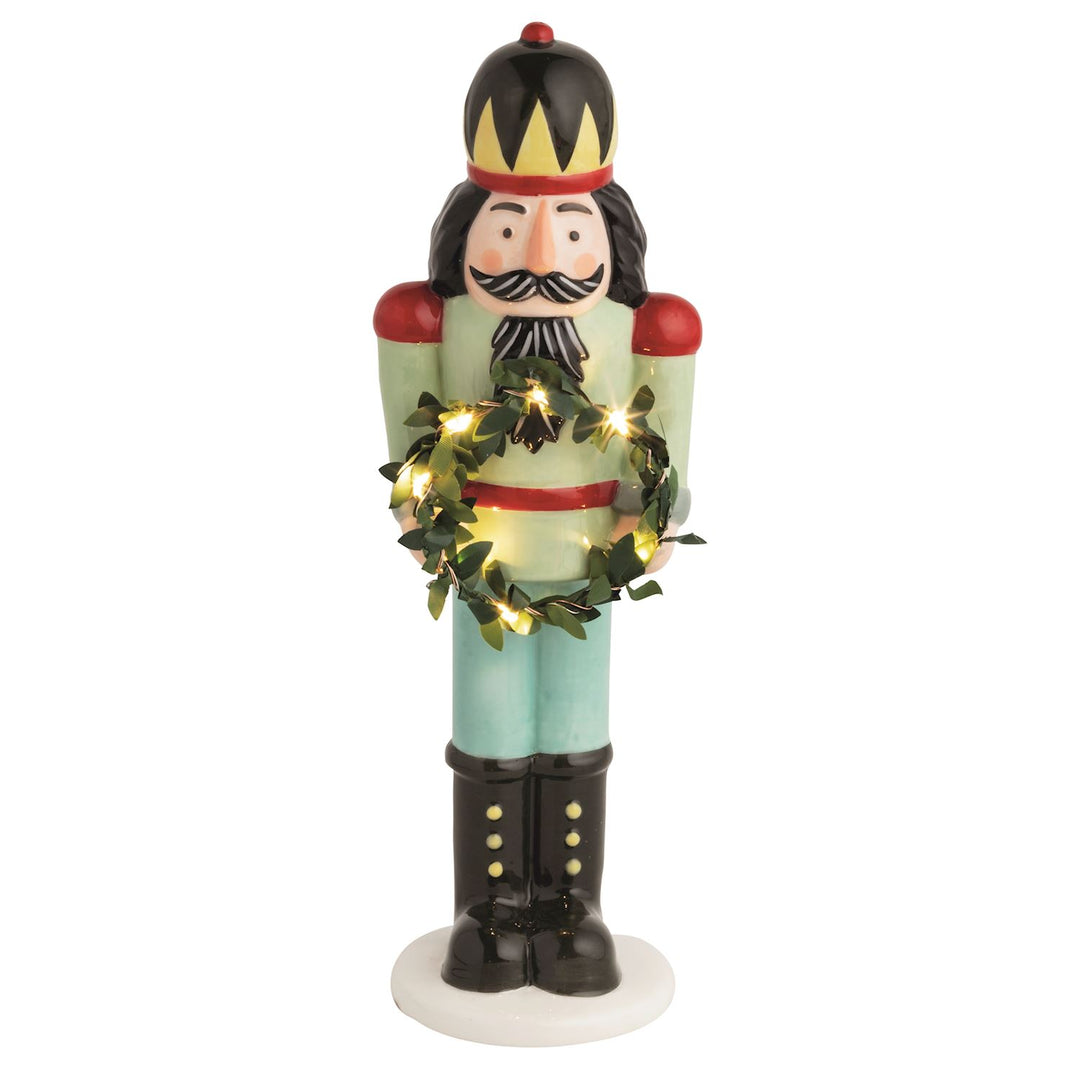 Hand-painted ceramic nutcracker holds light-up faux wreath. Batteries included.