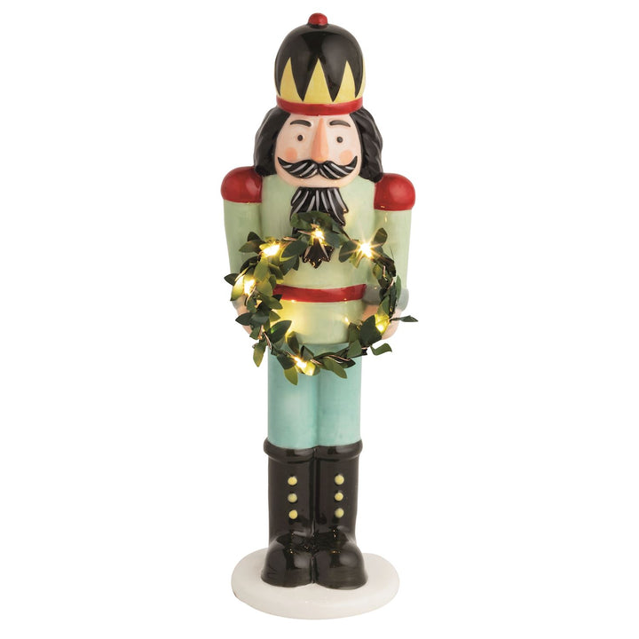 Hand-painted ceramic nutcracker holds light-up faux wreath. Batteries included.