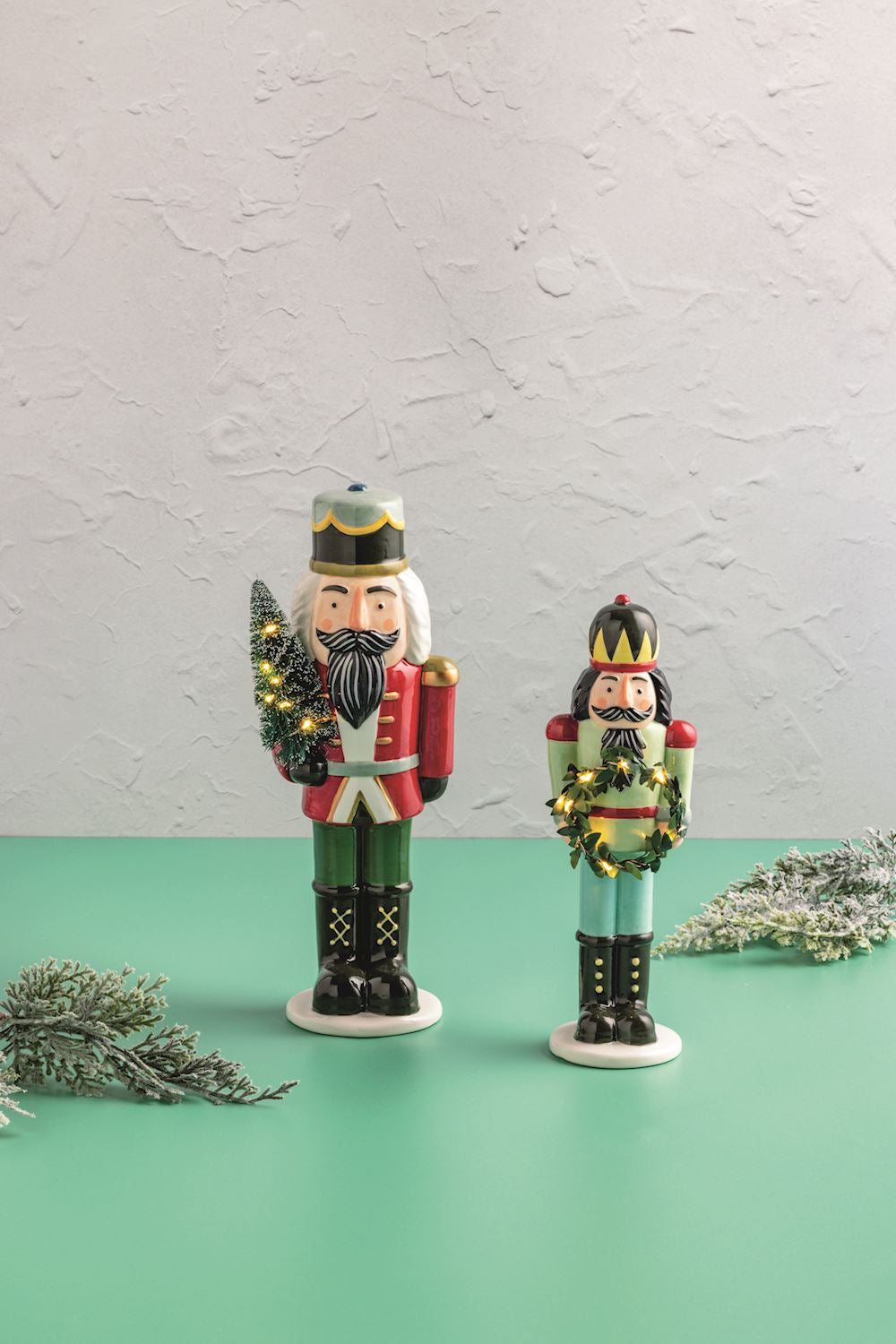 Two nutcrackers with Christmas decorations on a green surface and light gray background