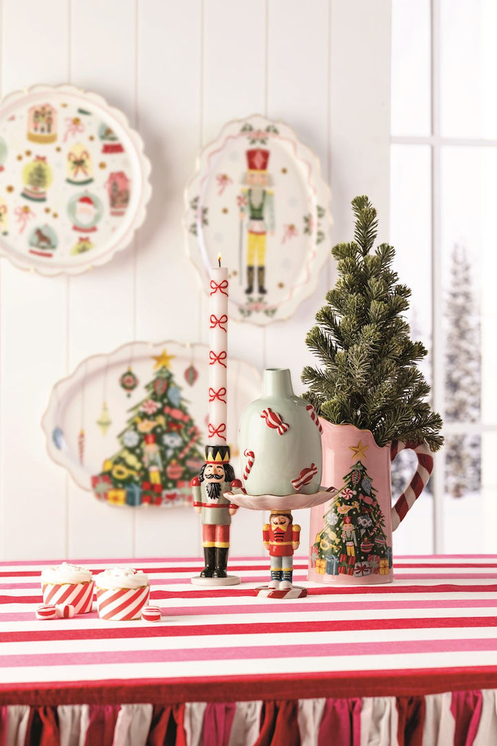 Decorative Christmas table setting with plates, vases, and small tree on a red and white striped tablecloth.