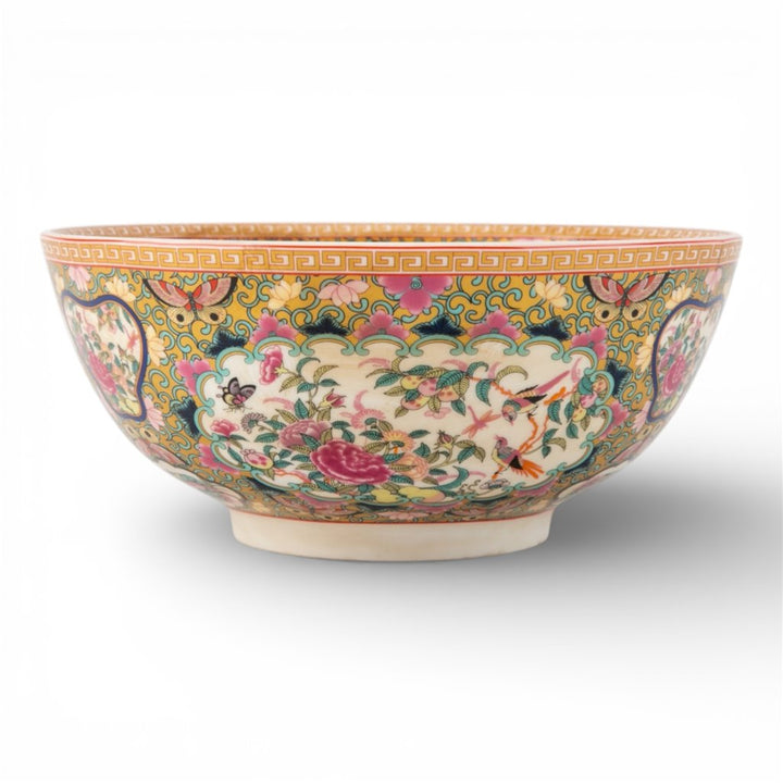 A decorative ceramic bowl featuring a colorful, intricate hand-painted floral and bird pattern on a yellow and green background, set against a plain white studio background.