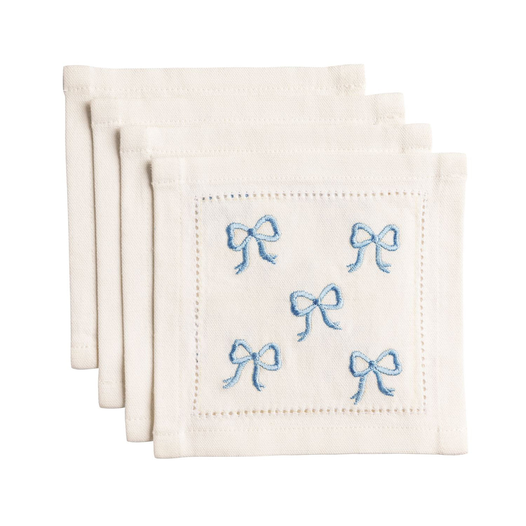 Set of white cocktail napkins with blue embroidered bows on a white background