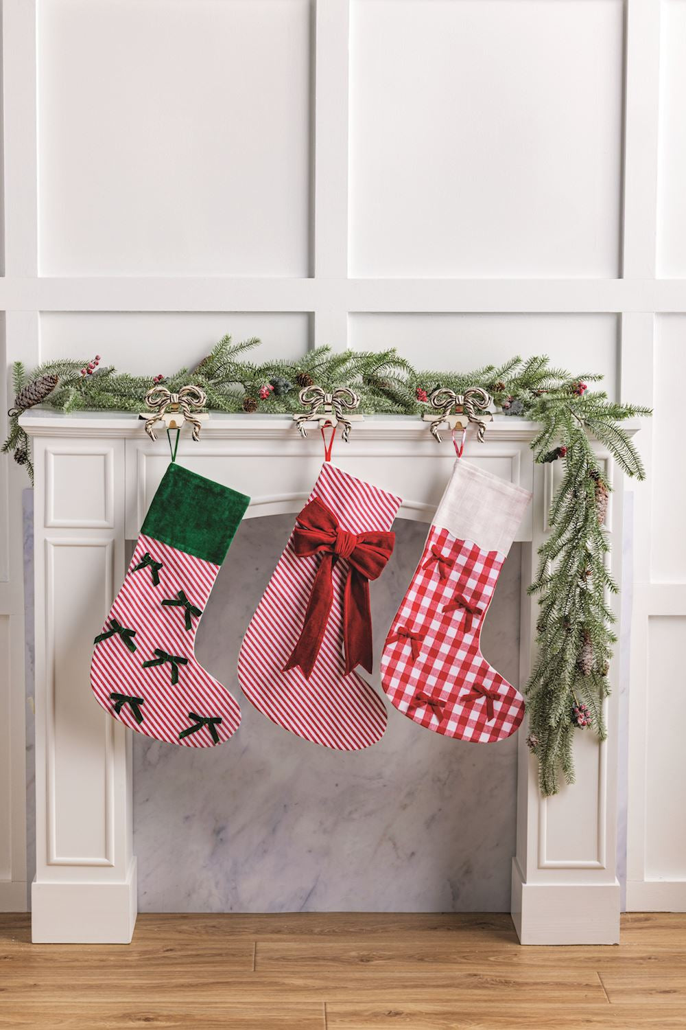 Three Christmas stockings hanging on a fireplace mantel with decorative garland.