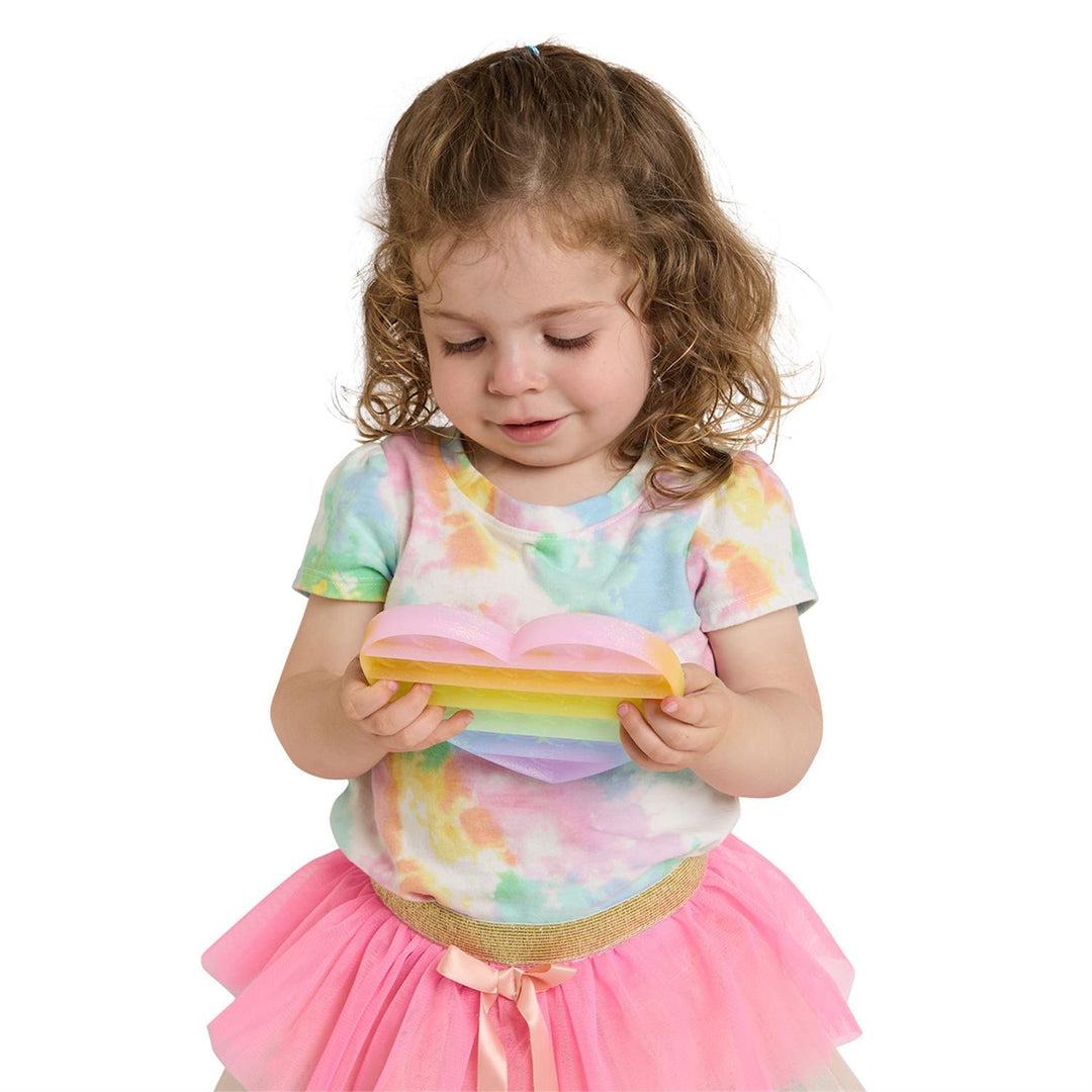 Child wearing a colorful tie-dye shirt and pink skirt holding a yellow object.