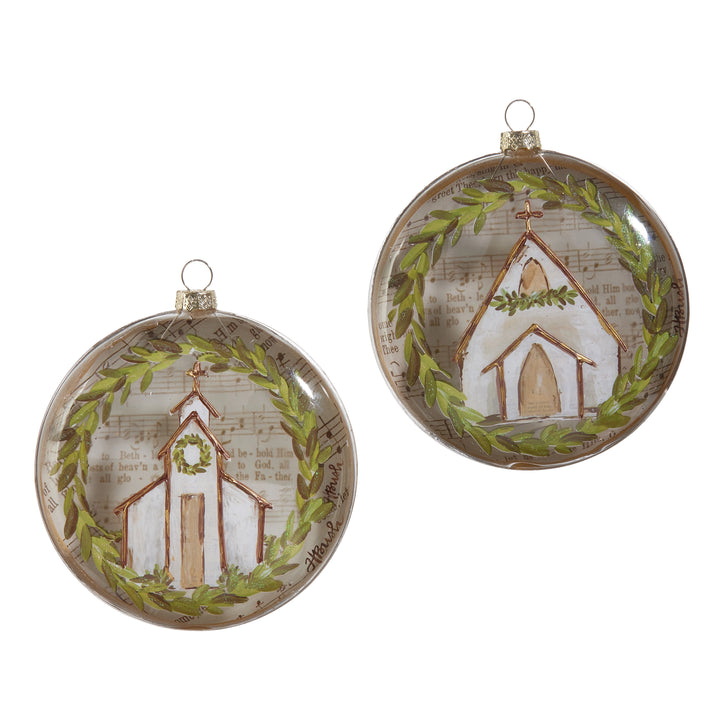 Two round glass Christmas ornaments featuring a hand-painted white church with a green wreath, set against a background of vintage sheet music.