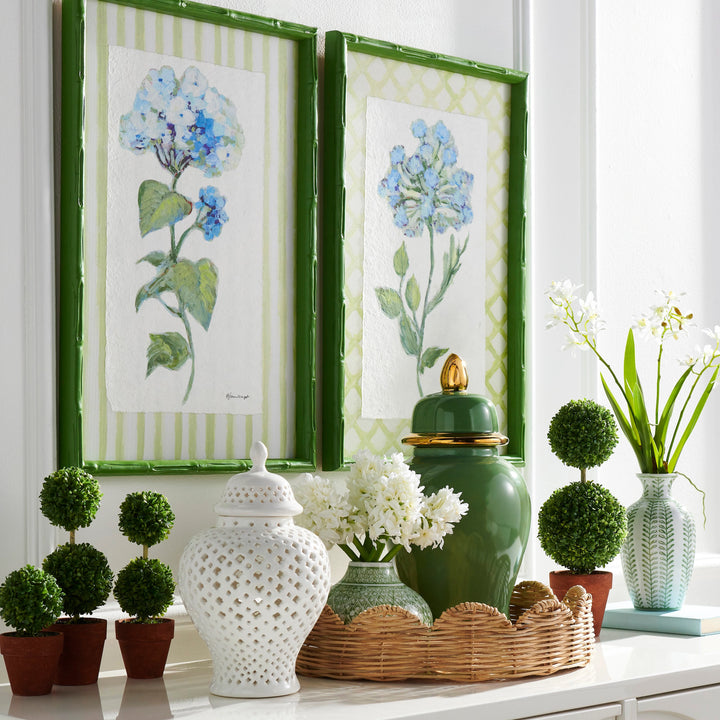 Decorative setting with floral prints, green vases, and potted plants on a white surface.