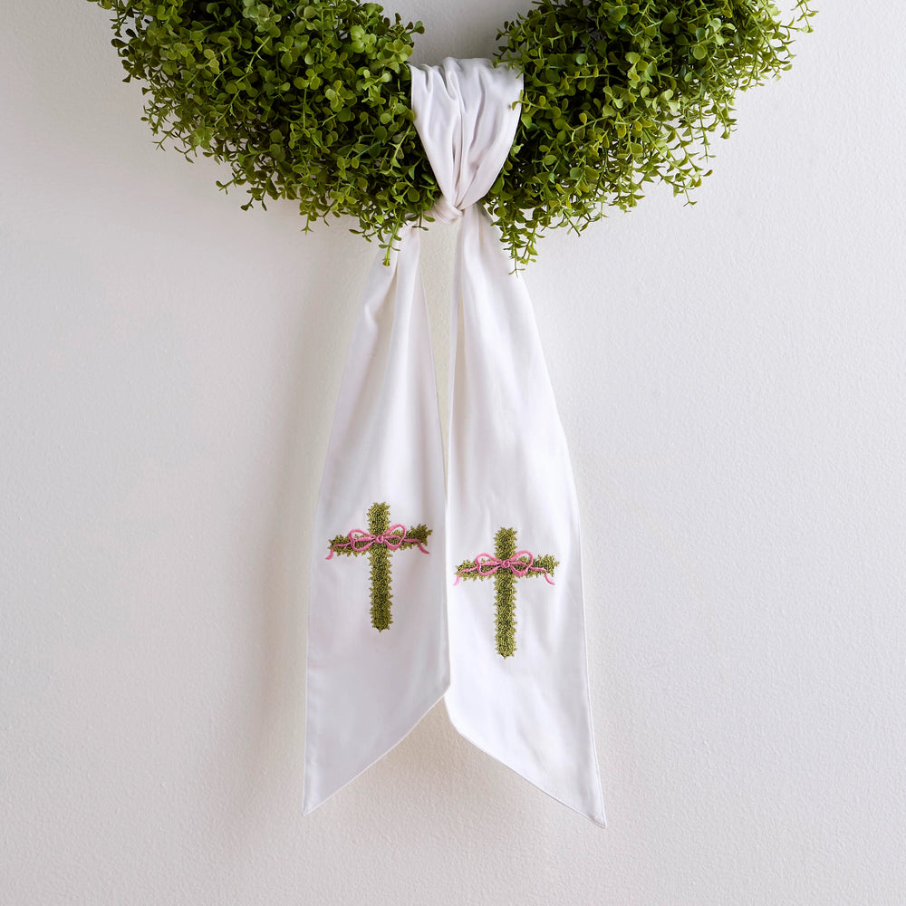 White fabric with embroidered crosses and ribbons, hanging against a white background