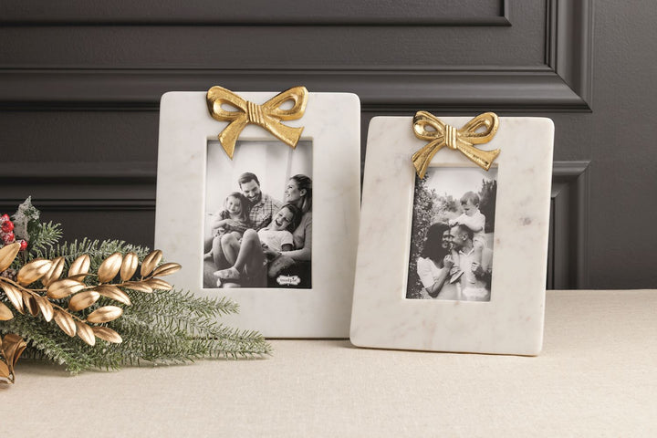 TWO WHITE MARBLE PICTURE FRAMES WITH GOLD BOWS ON TOP ON TABLE 