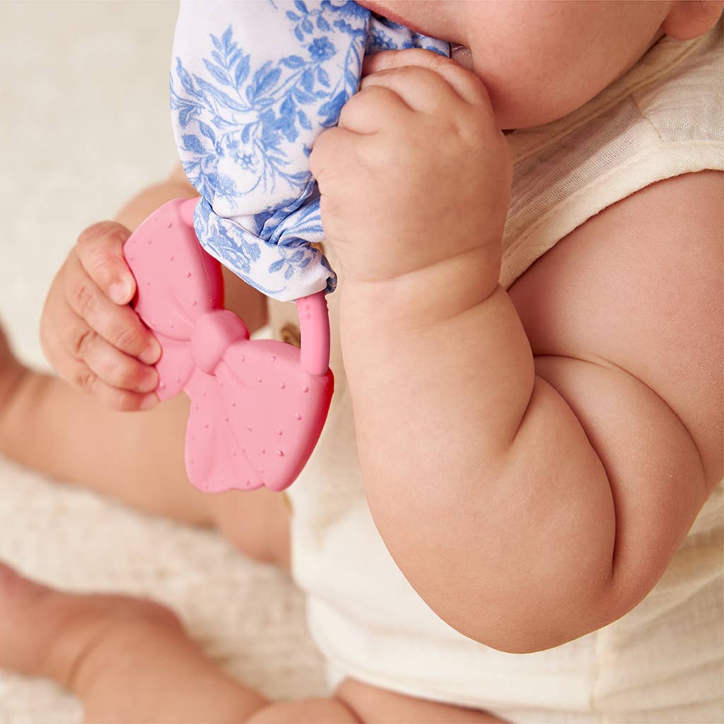 Baby holding a pink teething toy with a white and blue patterned cloth.