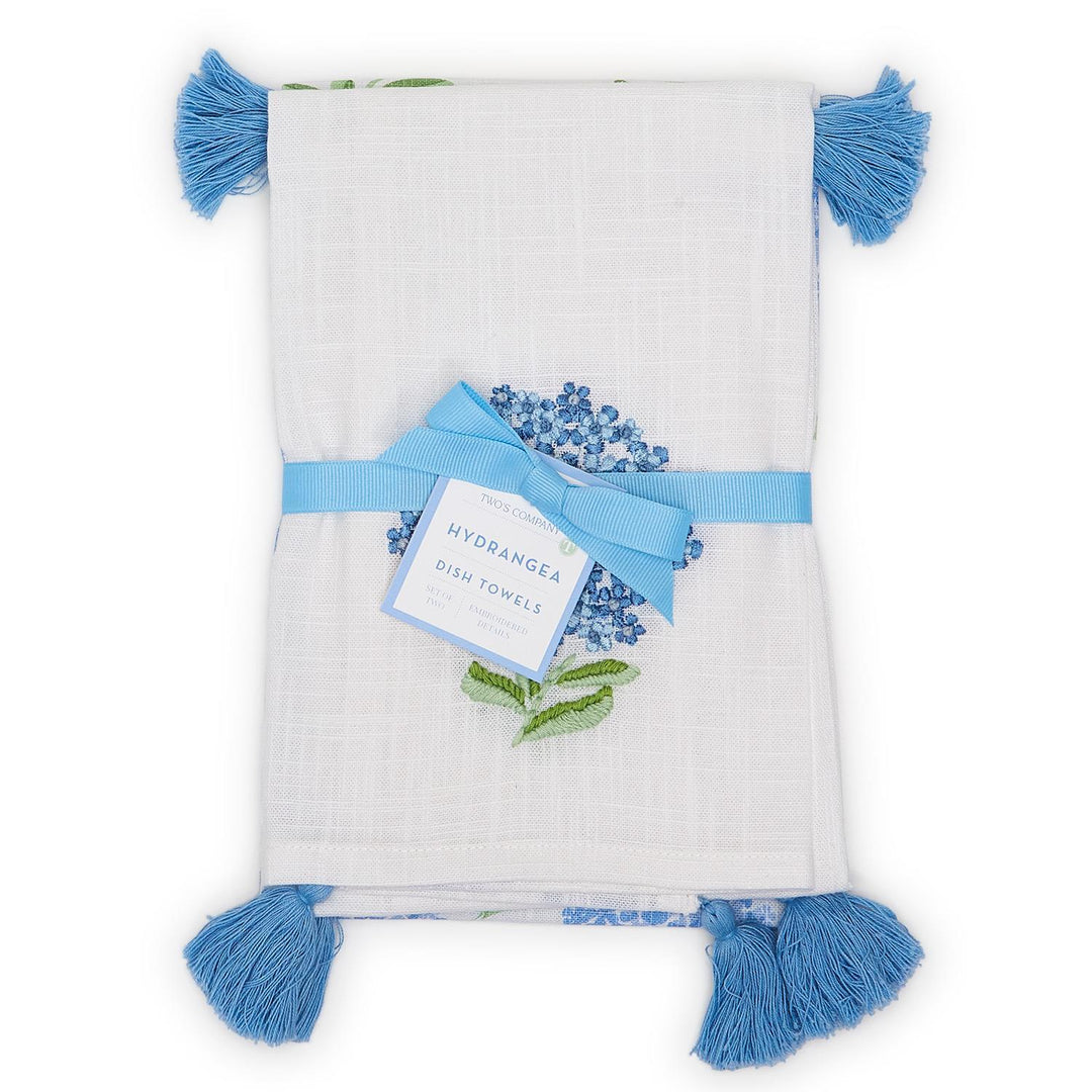White towel with blue tassels and floral design, featuring a tag labeled 'Hypanthea'.