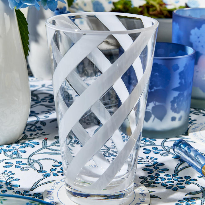 Clear glass with white decorative stripes on a table with blue and white patterned tablecloth.