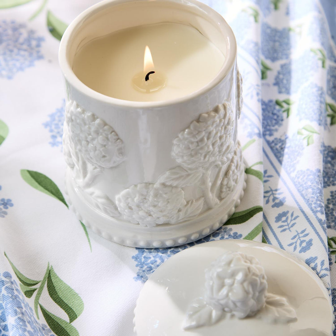 White embossed candle jar with a lit candle on a floral fabric background