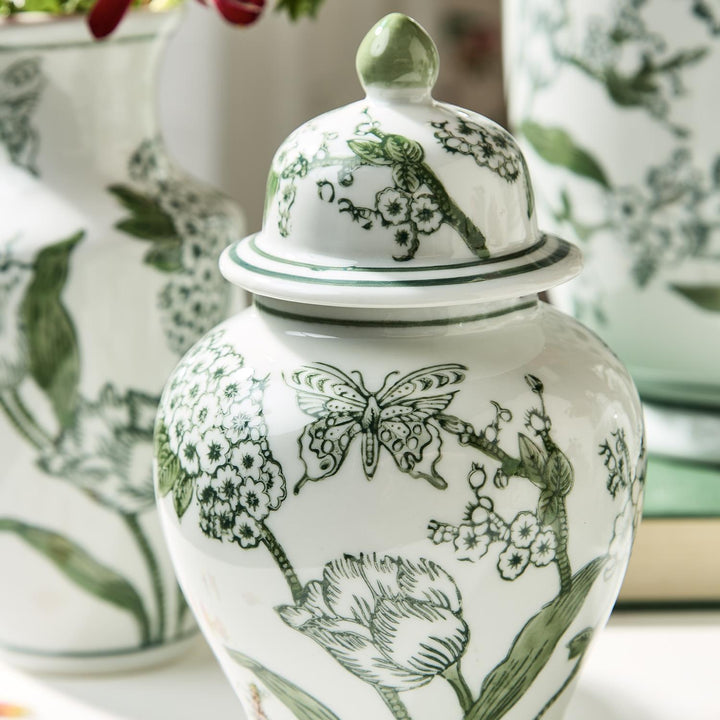 White ceramic jar with green floral and butterfly patterns on a blurred floral background