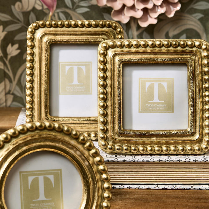 Three gold picture frames with decorative beads on a surface with floral background