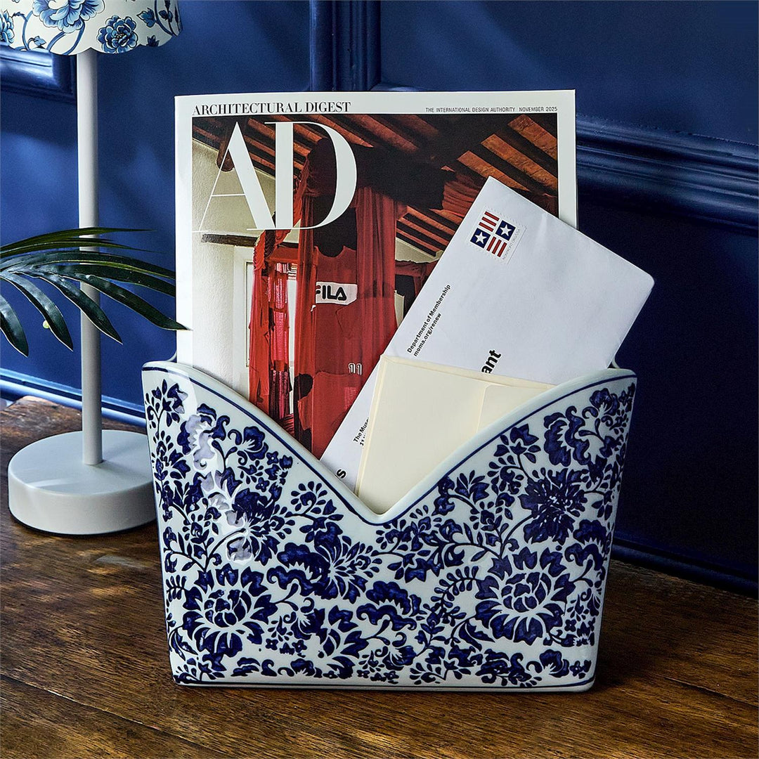 Decorative blue and white patterned magazine holder with mail and a magazine on a wooden surface.