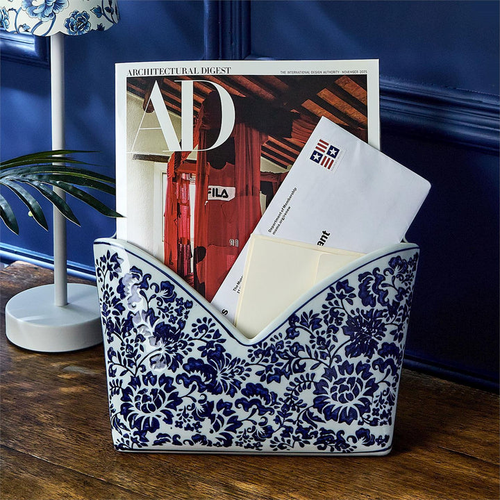Decorative blue and white patterned magazine holder with mail and a magazine on a wooden surface.