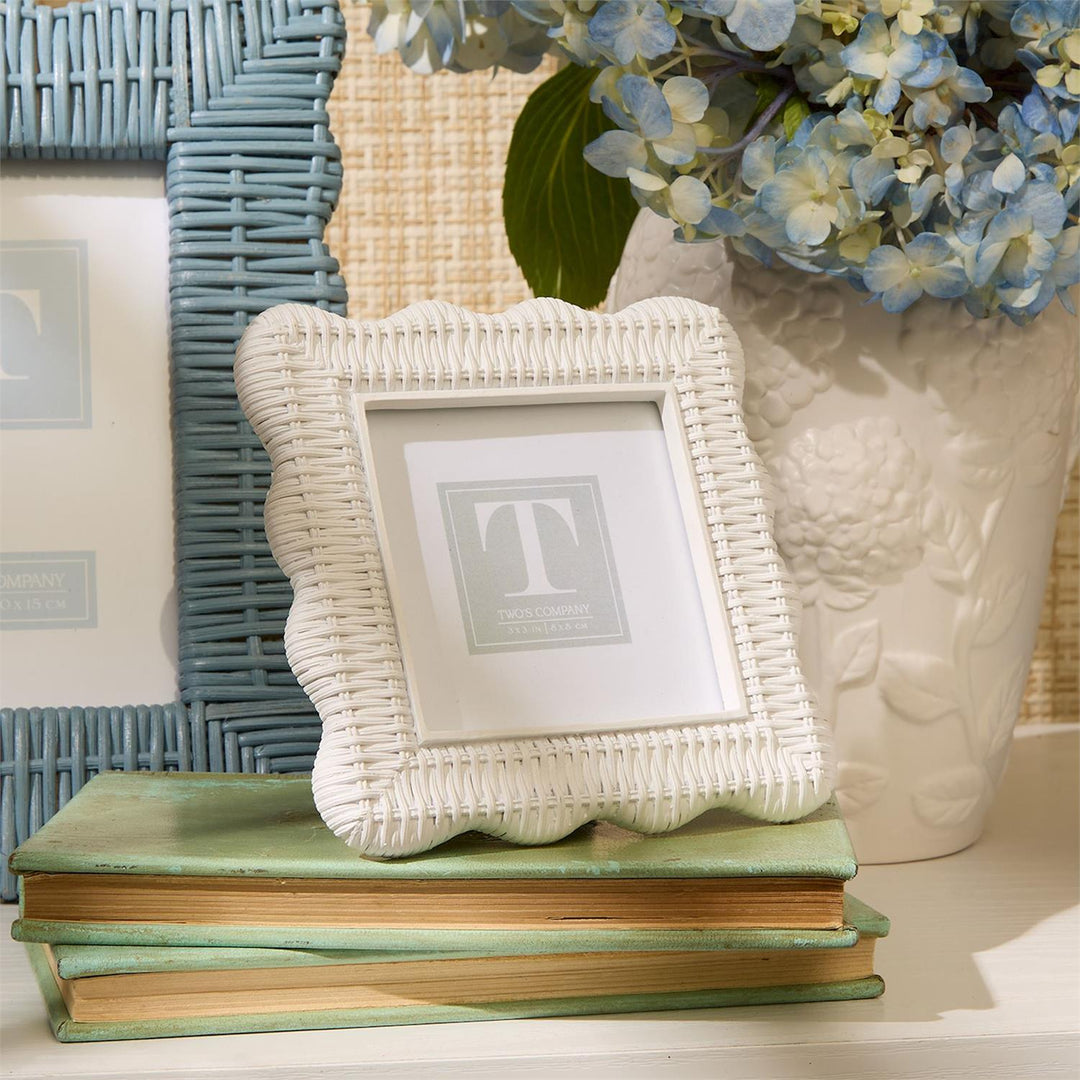 White wicker picture frame on a stack of books with a vase of blue flowers in the background