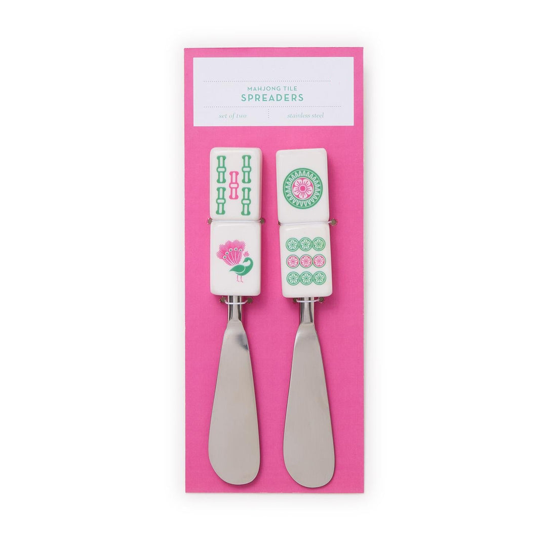 Two metal spreaders with decorative handles on a pink background