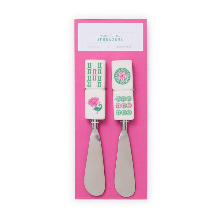 Two metal spreaders with decorative handles on a pink background