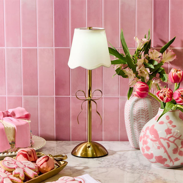 Decorative table setting with a lamp, flowers, and pastries against a pink tiled wall.