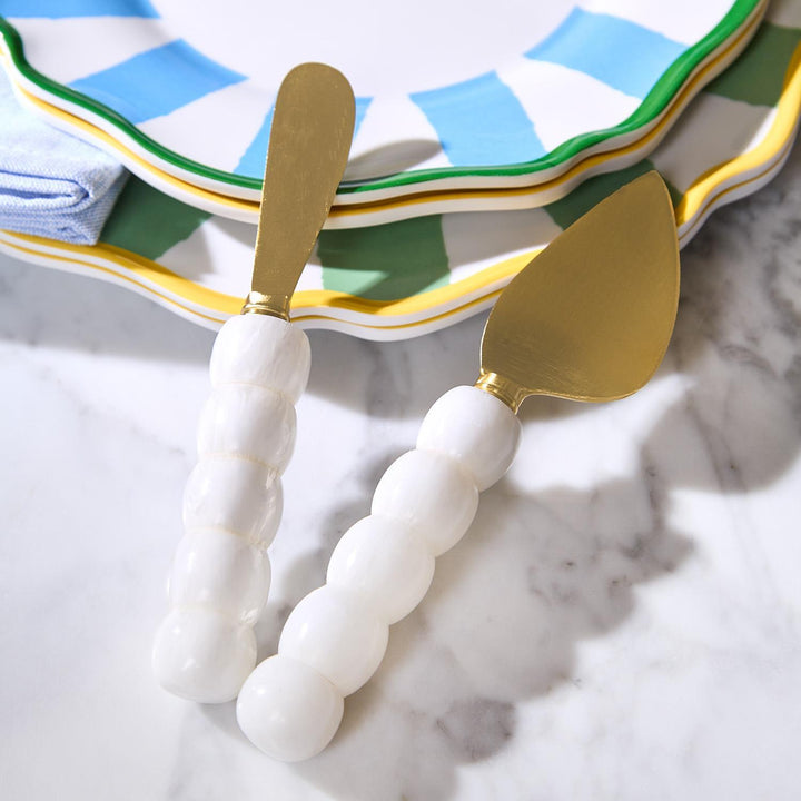 Two cake knives with white handles and gold blades on a marble surface.