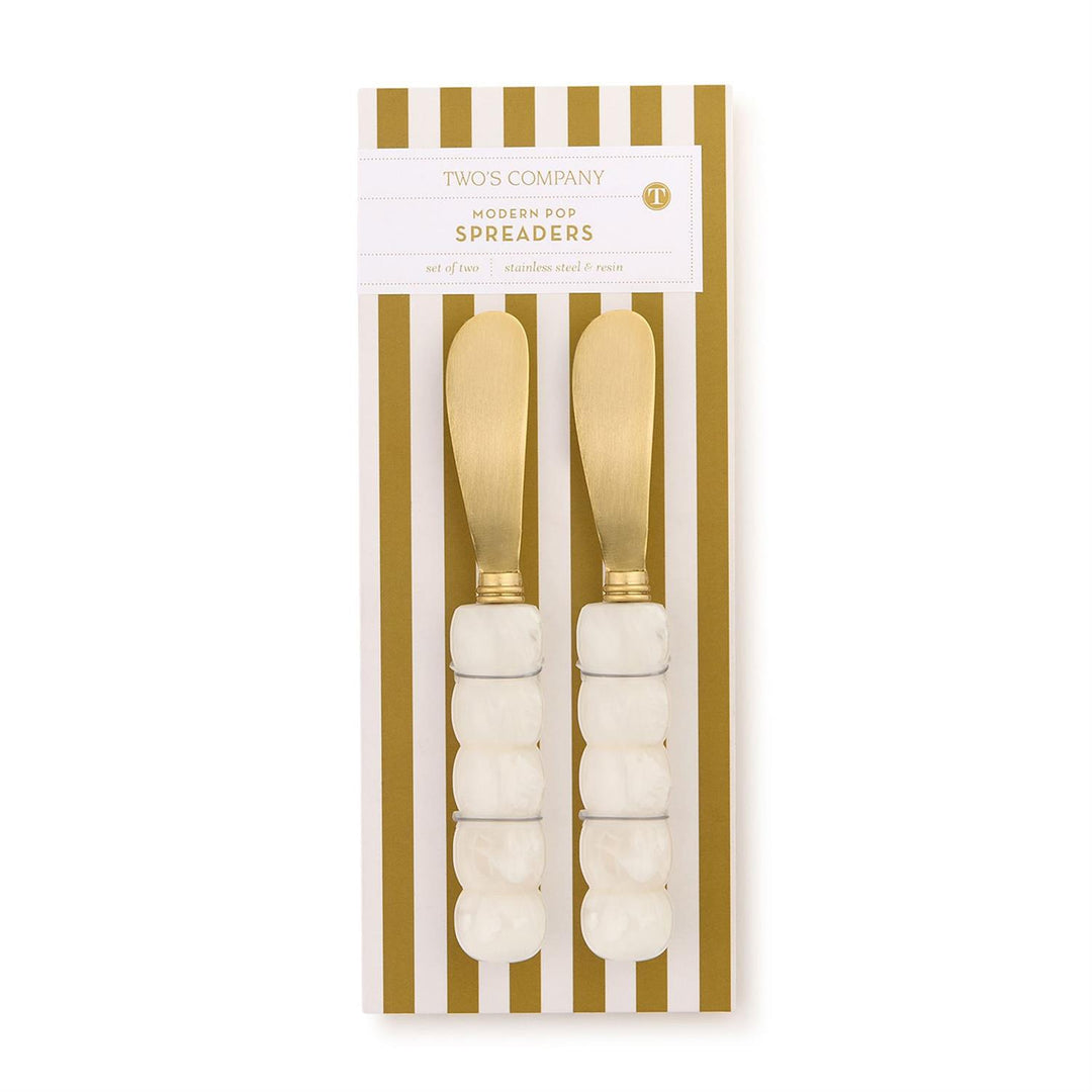 Packaged set of gold spreaders with white handles on a gold and white striped background