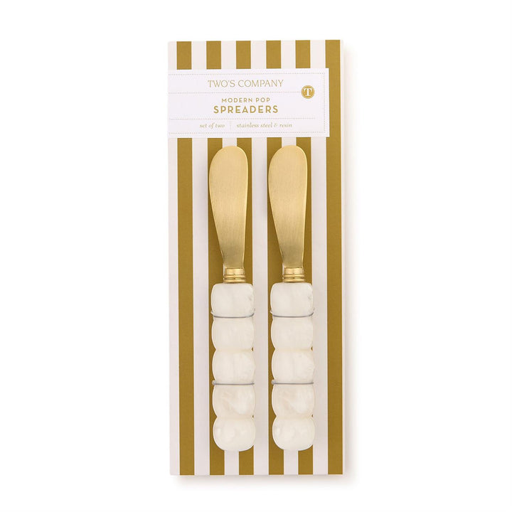 Packaged set of gold spreaders with white handles on a gold and white striped background