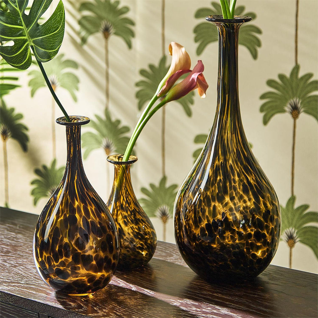 Three tortoiseshell patterned vases with flowers on a wooden surface against a decorative wall.