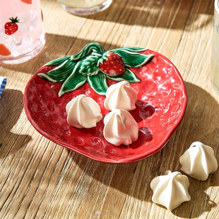 Red plate with strawberry design holding meringues on a wooden surface