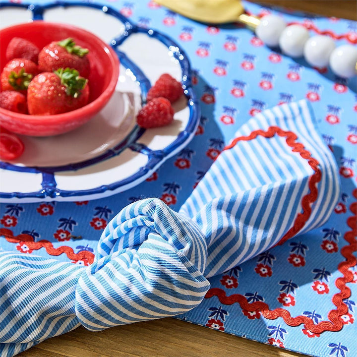 Blue and white striped napkin on a table with strawberries and a red bowl.