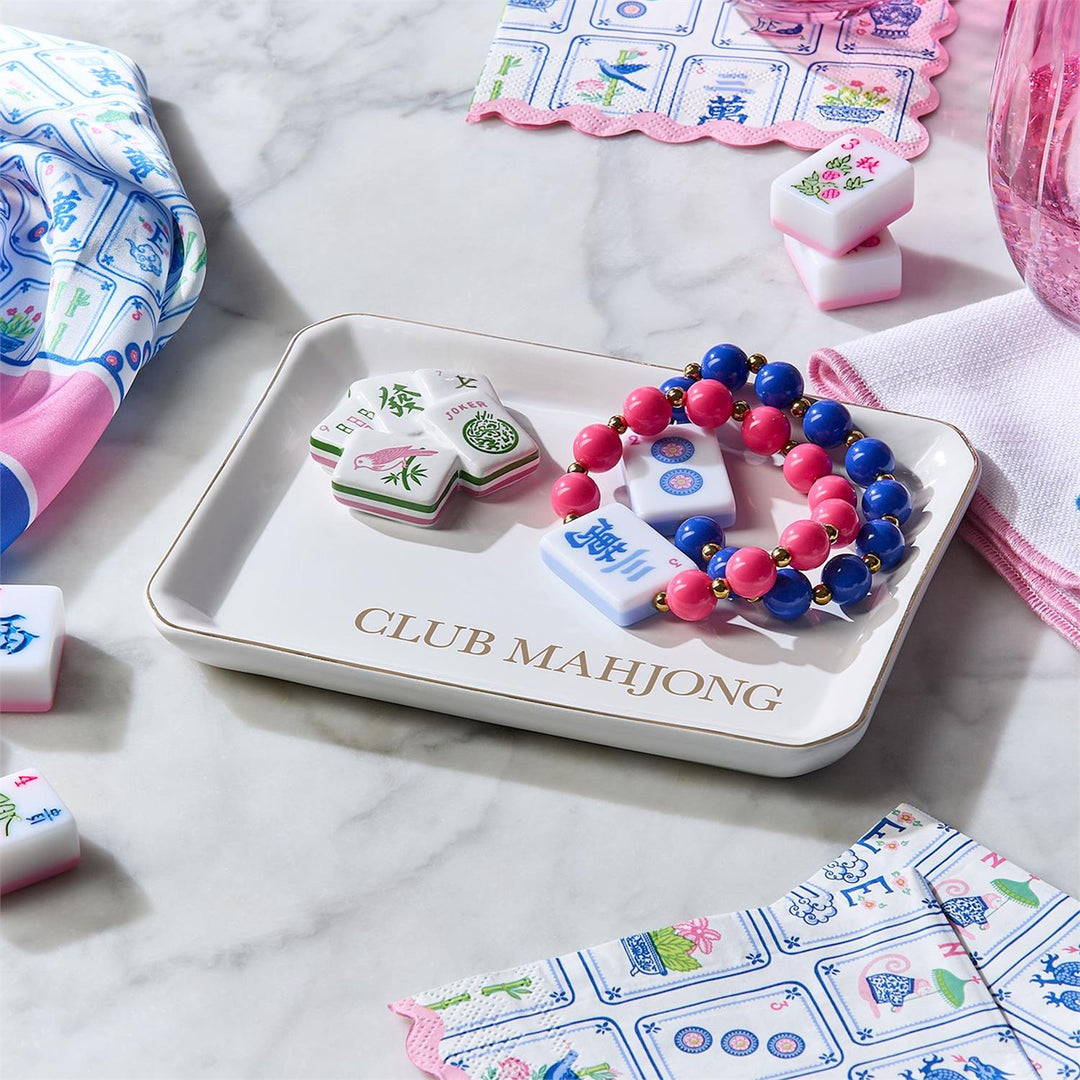Mahjong tiles on a tray with colorful beads, surrounded by game pieces and cards on a marble surface.