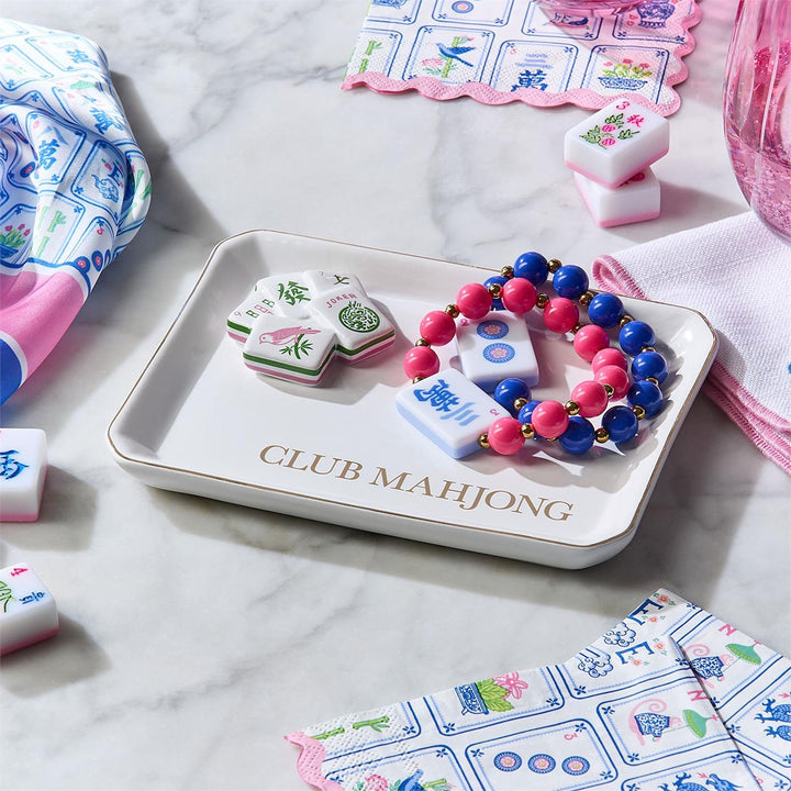 Mahjong tiles on a tray with colorful beads, surrounded by game pieces and cards on a marble surface.