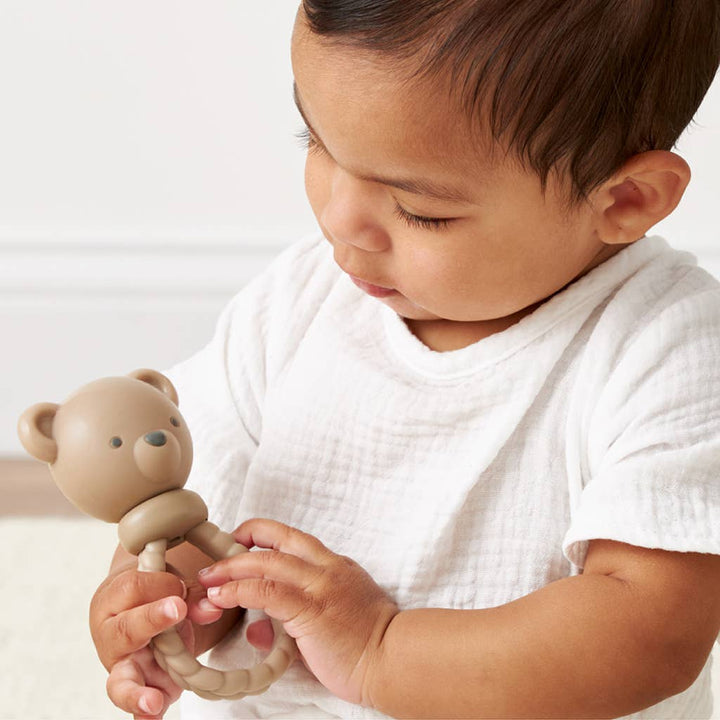 Baby holding a teddy bear rattle toy against a white background