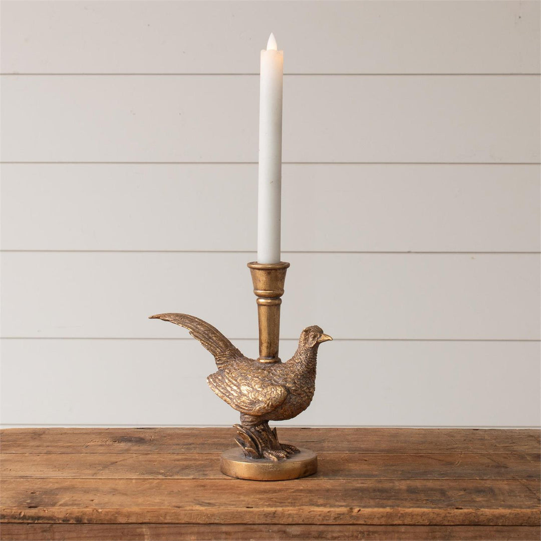 Bronze pheasant-shaped candle holder with a white candle on a wooden surface and light gray background
