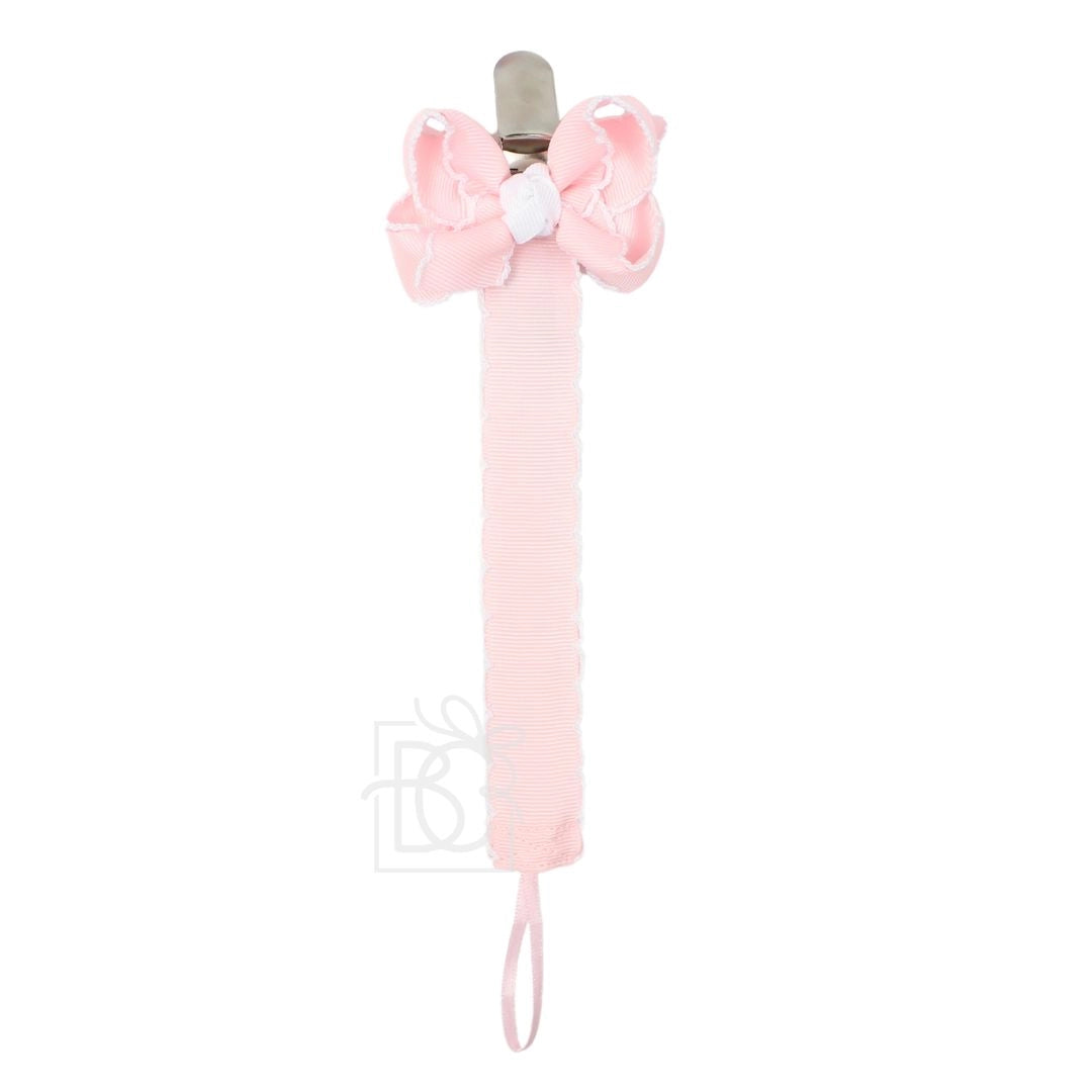 A light pink baby pacifier clip with a matching fabric bow on the top, a white decorative center, and a wrist strap at the bottom, shown against a plain white background.