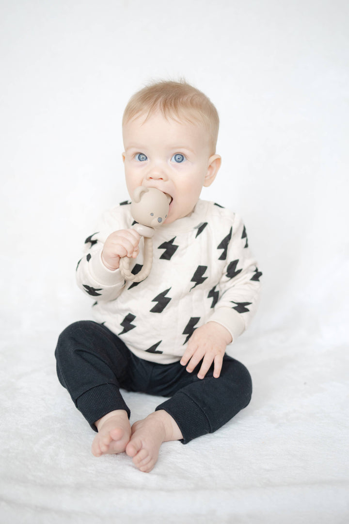 Baby wearing a black and white outfit with a pattern, sitting on a white surface.