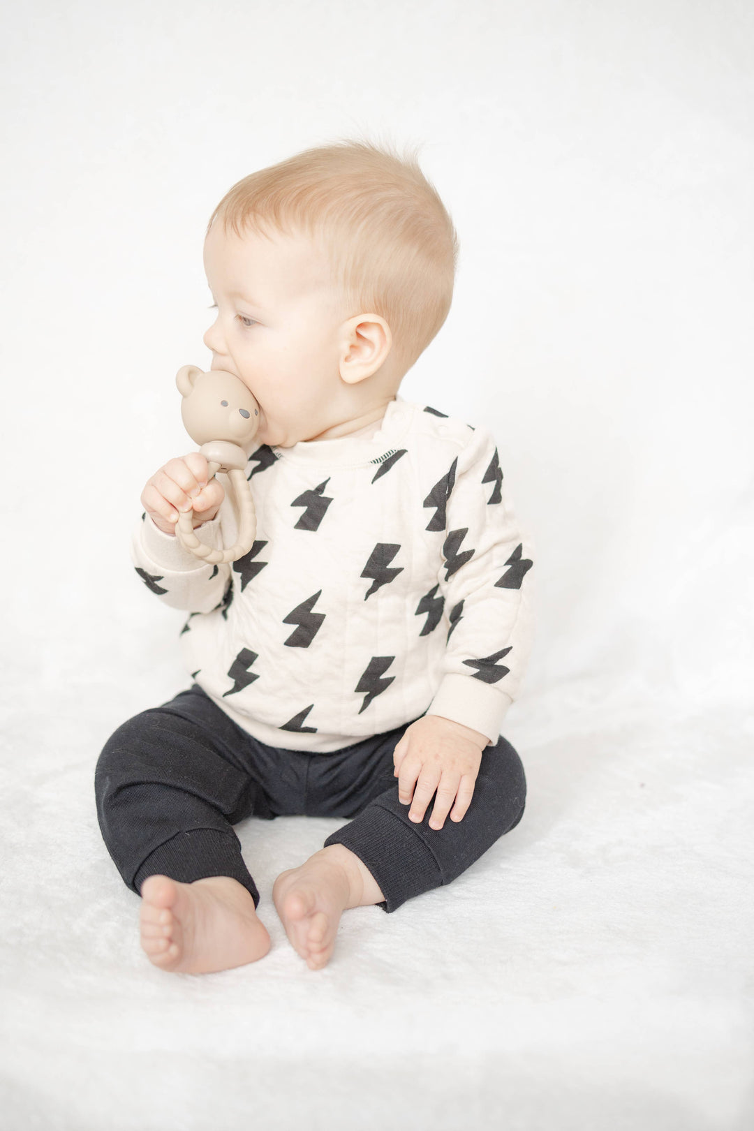Baby wearing a white sweater with black patterns and dark pants on a white background