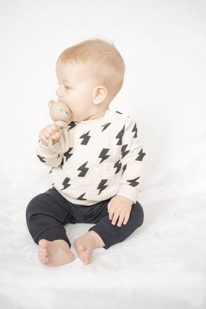 Baby wearing a white sweater with black patterns and dark pants on a white background