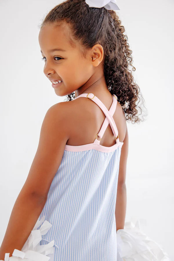 Young girl wearing a light blue and white striped dress with pink straps on a white background