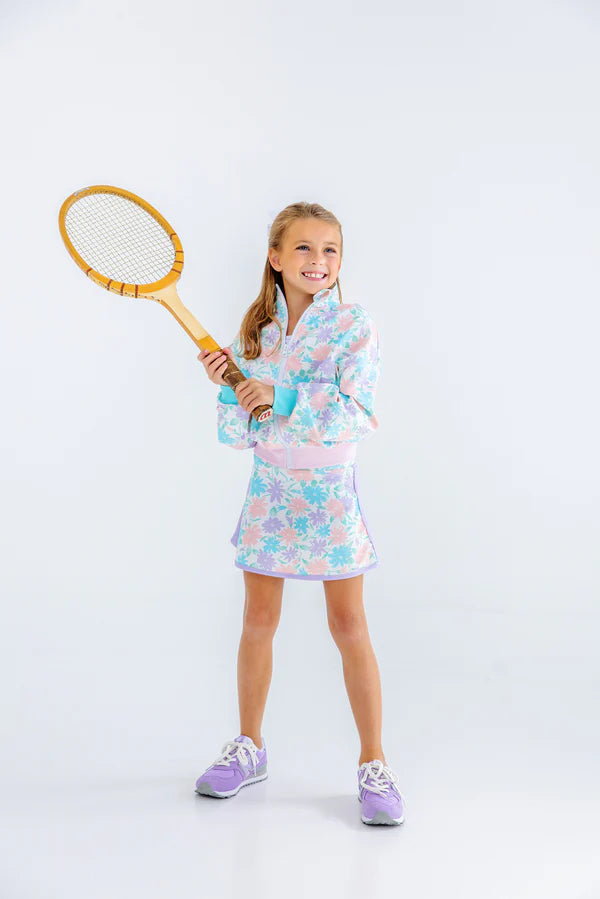 Young girl in a floral dress holding a tennis racket on a white background