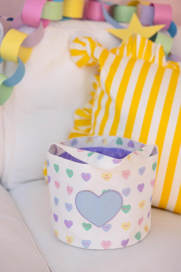 Children's toy storage basket with heart pattern on a white surface, surrounded by colorful toys.