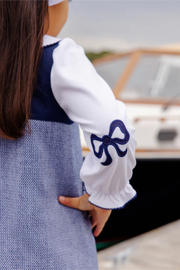 Person wearing a white long-sleeve shirt with a blue bow design, standing outdoors.