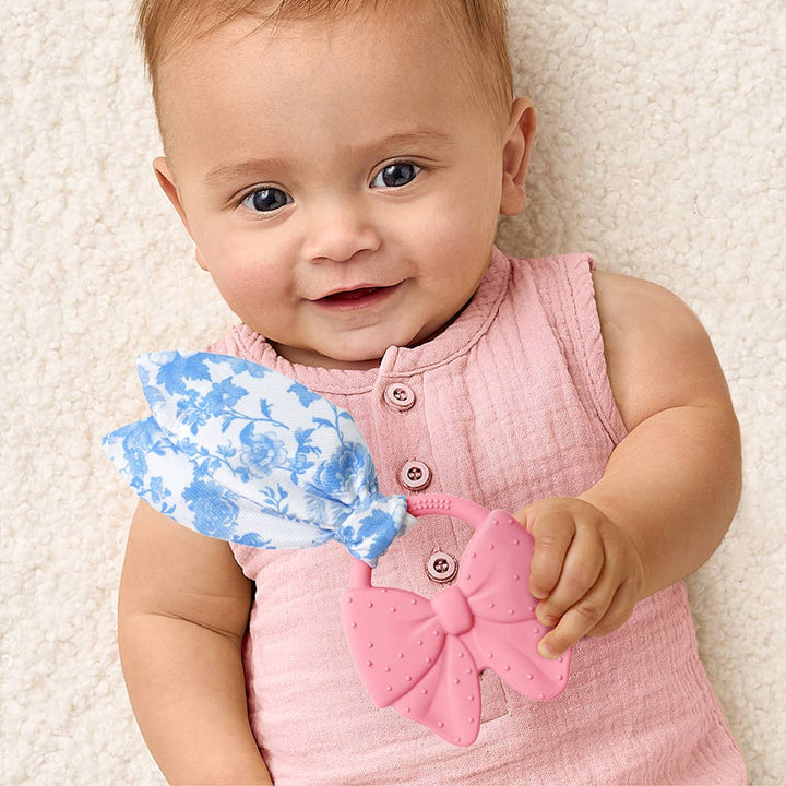 Baby holding bow shaped teether toy, on a light background.