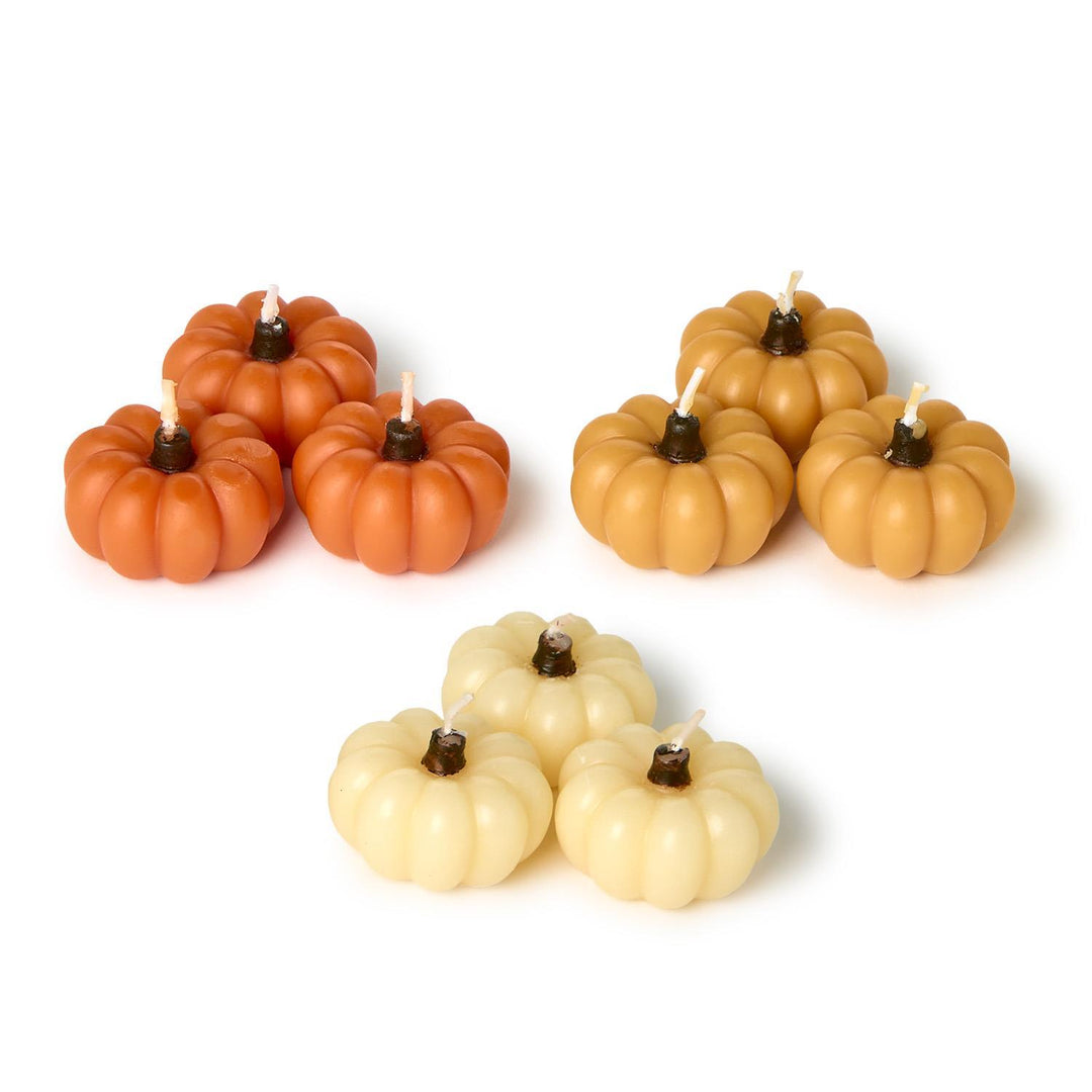 Set of pumpkin-shaped candles in orange, beige, and white on a white background