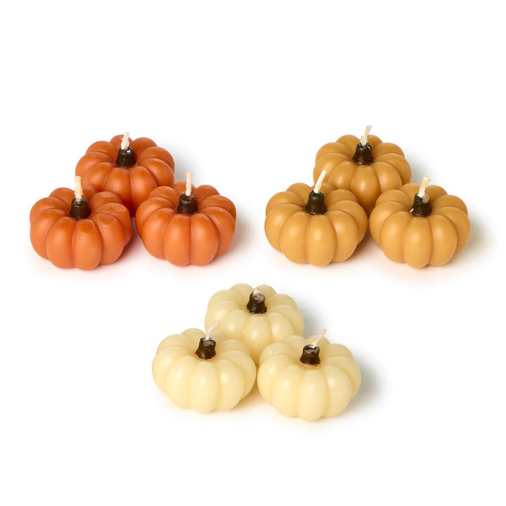 Set of pumpkin-shaped candles in orange, beige, and white on a white background