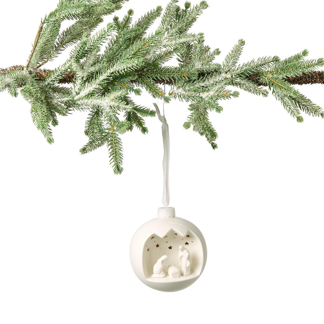 White Christmas ornament with cut-out design hanging from a tree branch.