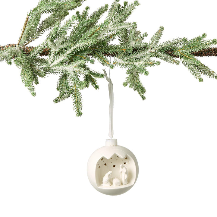 White Christmas ornament with cut-out design hanging from a tree branch.